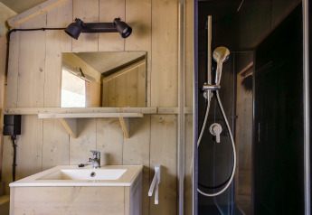 Bathroom inside safari tent 'De Bosvilla' at Gooise Heide, Netherlands, featuring shower, sink, and mirror.