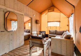 Cozy interior of a safari tent at De Bosvilla, Gooise Heide, Netherlands, with wooden furniture and soft sofas.