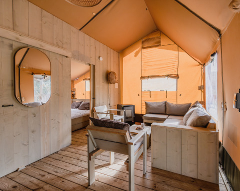 Gezellig interieur van safaritent De Bosvilla op Gooise Heide, Nederland, met houten meubilair en zachte bank.