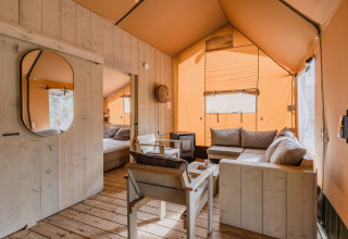 Gezellig interieur van safaritent De Bosvilla op Gooise Heide, Nederland, met houten meubilair en zachte bank.