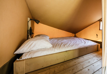 Interior shot of cozy sleeping area with a bed and reading lamp in the safari tent 'De Bosvilla' at Gooise Heide.