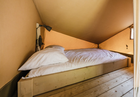 Slaapgedeelte met comfortabel bed en leeslamp in safaritent ‘De Bosvilla’ op de Gooise Heide, Nederland.