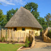 Charming glamping lodge with thatched roof and wooden fence at Zoo Schwerin Loewenlodge, Nedersaksen, amid greenery.
