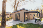 Chalet glamping moderno con rivestimento in legno, patio coperto e mobili da esterno in un giardino soleggiato.