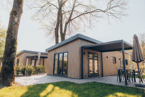 Alloggio glamping moderno con rivestimento in legno, ampie vetrate e patio immerso nella natura.