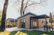 Alloggio glamping moderno con rivestimento in legno, ampie vetrate e patio immerso nella natura.