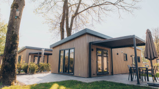 Alloggio glamping moderno con rivestimento in legno, ampie vetrate e patio immerso nella natura.