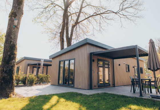 Moderne glamping accommodatie met houten gevel, grote ramen en terras in een groene, natuurlijke omgeving.