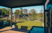 Vista dalla terrazza della Loevestein Comfort lodge a Veluwe park de Bosgraaf, Paesi Bassi, su stagno e giardino.