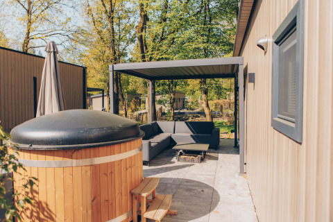 Outdoor area of Loevestein Deluxe lodge at Veluwe park de Bosgraaf, featuring hot tub and shaded patio.