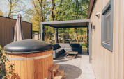 Outdoor area of Loevestein Deluxe lodge at Veluwe park de Bosgraaf, featuring hot tub and shaded patio.