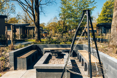 Outdoor seating area with benches, fire pit, and grill at Loevestein Deluxe, Veluwe park de Bosgraaf, Netherlands.