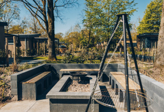 Outdoor seating area with benches, fire pit, and grill at Loevestein Deluxe, Veluwe park de Bosgraaf, Netherlands.