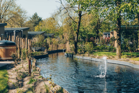 Vue sur un étang avec fontaine et des lodges modernes dans un cadre verdoyant au Loevestein Deluxe.