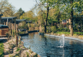 Scenic view of a pond with a fountain and modern lodges surrounded by greenery at Loevestein Deluxe.