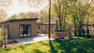 Loevestein Comfort Lodge mit moderner Terrasse, grünem Rasen und privatem Hot Tub im Sonnenschein.