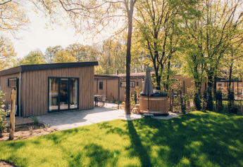 Loevestein Comfort Lodge mit moderner Terrasse, grünem Rasen und privatem Hot Tub im Sonnenschein.