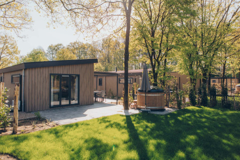 Lodge Loevestein Comfort avec terrasse ensoleillée, pelouse verte et bain à remous extérieur privé.