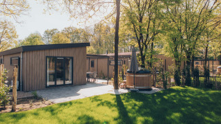 Lodge Loevestein Comfort con terraza soleada, césped verde y bañera de hidromasaje privada exterior.