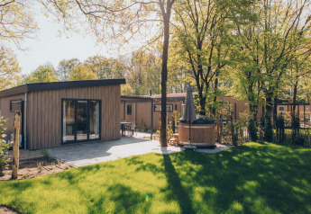 Lodge Loevestein Comfort con terraza soleada, césped verde y bañera de hidromasaje privada exterior.