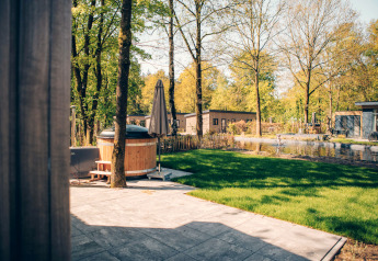 Vista de terraza con jacuzzi y estanque en Loevestein Comfort, Veluwe park de Bosgraaf, Países Bajos, en un día soleado.