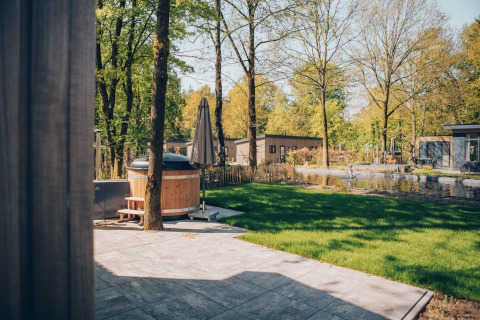 View of patio with hot tub and pond at Loevestein Comfort, Veluwe park de Bosgraaf, Netherlands, on a sunny day.