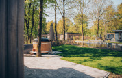 View of patio with hot tub and pond at Loevestein Comfort, Veluwe park de Bosgraaf, Netherlands, on a sunny day.