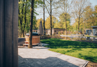 Vista de terraza con jacuzzi y estanque en Loevestein Comfort, Veluwe park de Bosgraaf, Países Bajos, en un día soleado.