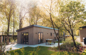Das Loevestein-Lodge mit Whirlpool, von grünen Bäumen umgeben, mit moderner Terrasse im Sonnenschein.