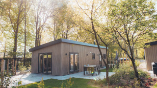 Loevestein lodge with hot tub, surrounded by trees, featuring outdoor seating and bathed in sunlight.