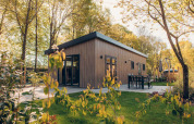 Ein modernes Holzhaus in Veluwe Park de Bosgraaf, Niederlande, mit Terrasse und Gartenmöbeln im Grünen.