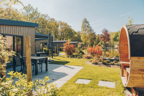 Giornata soleggiata al lodge Loevestein Deluxe nel parco Veluwe de Bosgraaf, patio e sauna a botte visibili.