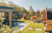 Sunny day at Loevestein Deluxe lodge in Veluwe park de Bosgraaf, Netherlands, patio and barrel sauna shown.