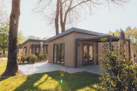 Photo d’un hébergement glamping moderne avec extérieur en bois et terrasse, situé dans une zone boisée.