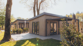 Photo of a modern glamping accommodation with a wooden exterior and terrace in a scenic woodland area.