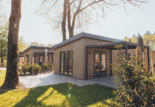 Foto van een moderne glampingaccommodatie met houten gevel en terras in een natuurlijke bosrijke omgeving.