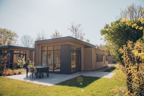 Moderno lodge a Cannenburch con ampie vetrate, patio e mobili da giardino circondati dal verde.