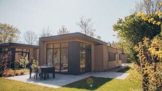 Moderno lodge a Cannenburch con ampie vetrate, patio e mobili da giardino circondati dal verde.