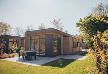 Moderno lodge a Cannenburch con ampie vetrate, patio e mobili da giardino circondati dal verde.