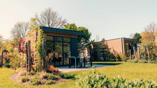 Outdoor view of Cannenburch lodge at Veluwe park de Bosgraaf, Netherlands, surrounded by green landscape.