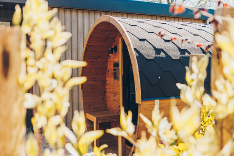 Outdoor photo of a barrel-shaped wooden sauna at Batenburgh lodge, Veluwe park de Bosgraaf in the Netherlands.