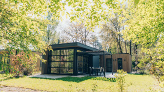 Lodge Bosvilla Comfort moderno circondato da alberi verdi lussureggianti e un tranquillo giardino soleggiato.
