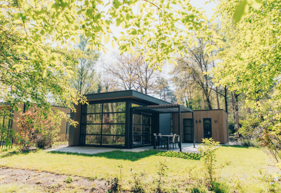 Bosvilla Comfort-Lodge mit moderner Architektur in einem grünen, sonnigen Waldgebiet im Frühling.
