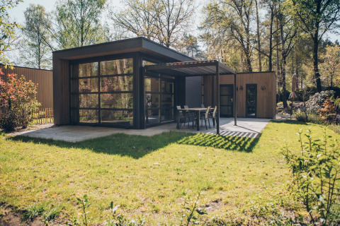 Moderne Bosvilla Comfort-lodge in Veluwe park de Bosgraaf met grote ramen, terras en een groene tuin.