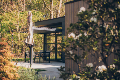 Terrasse mit Tisch, Stühlen und Sonnenschirm bei Bosvilla Comfort im Veluwe Park de Bosgraaf, Niederlande.