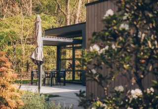 Terraza con mesa, sillas y sombrilla cerrada en Bosvilla Comfort del parque Veluwe de Bosgraaf, Países Bajos.