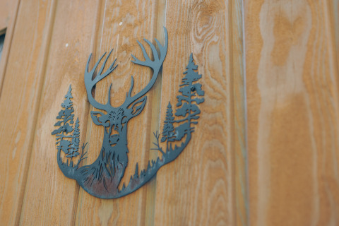 Metallrelief mit Hirsch und Bäumen an einer Holztür bei Bosvilla Comfort, Veluwe park de Bosgraaf, Niederlande.