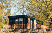 Moderne lodge Valkhof med hottub, omgivet af grønne træer og sollys, indbyder til afslapning i naturen.