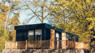 Lodge moderno Valkhof con jacuzzi, rodeado de árboles verdes y sol, perfecto para relajarse en la naturaleza.