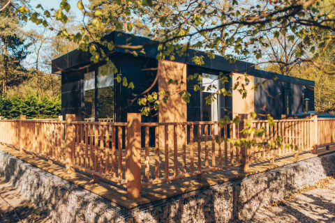 Moderna cabaña con terraza de madera y barandilla, en el parque Veluwe de Bosgraaf, Países Bajos.